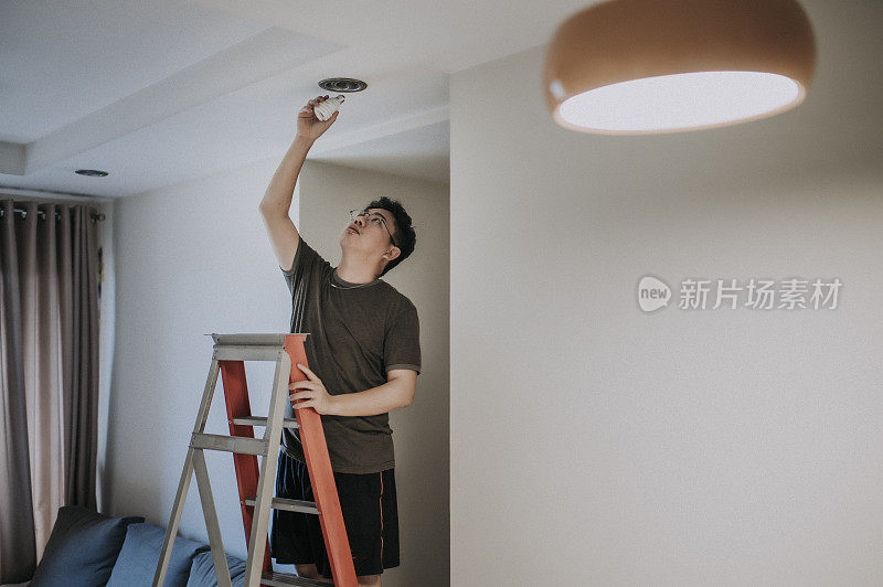 an asian chinese mid adult male changing light bulb in living room, apartment home